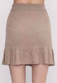 Strickrock in Beige mit gerippter Textur und einem ausgestellten Spitzenrand, der ein Diamantmuster aufweist. Elastischer Bund für eine taillierte Silhouette.