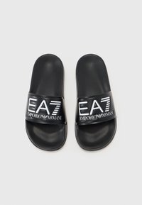 Črne slape z teksturirano površino, ki imajo širok trak z belim napisom "EA7 Emporio Armani".