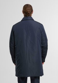 Marineblauer langer Mantel mit gestepptem Material, ausgeprägtem Kragen und langen Ärmeln. Aus glattem Stoff mit leicht glänzender Oberfläche.