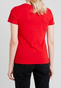 Red cotton t-shirt with short sleeves and a crew neckline, featuring a smooth texture and a fitted cut, worn with black pants.