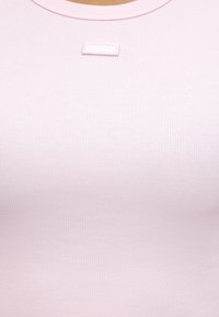 Tissu côtelé rose clair en gros plan avec une encolure ronde et une petite pièce rectangulaire cousue près du col.