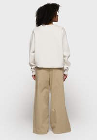 Felpa over-size color crema con spalle scese, abbinata a pantaloni larghi beige, tessuto morbido e design minimalista.