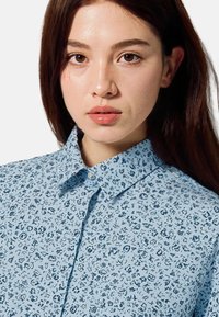 Lichtblauw overhemd met knopen en een bloemenpatroon in donkerblauw. Klassieke kraag, gladde textuur en subtiele details overal.