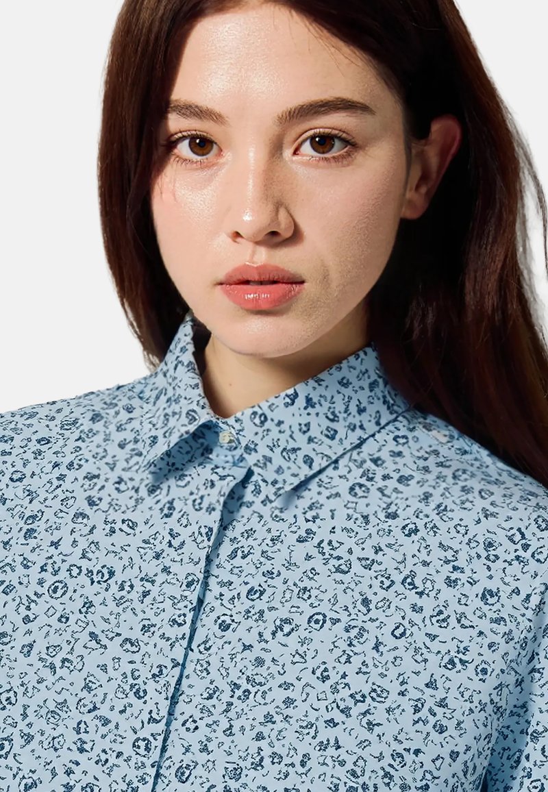 Lichtblauw overhemd met knopen en een bloemenpatroon in donkerblauw. Klassieke kraag, gladde textuur en subtiele details overal.