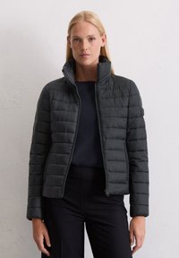 Mørk grå, quiltet puffjakke med høy krage og glidelås. Laget av lett, skinnende materiale med sidelommer.