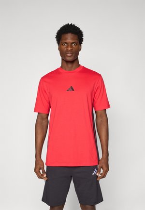 Rotes Sport-T-Shirt aus glattem Material, mit Rundhalsausschnitt und einem kleinen schwarzen Adidas-Logo in der Mitte. Kombiniert mit dunklen Shorts.