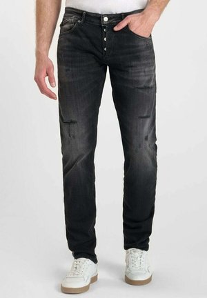 Jeans en denim noir à coupe slim, avec des détails de décoloration et d'usure, cinq poches et une fermeture à bouton sur le devant. Assortis à des sneakers blanches.