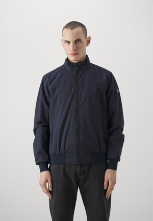 Marineblauwe lichtgewicht jas met een hoge kraag, een rits aan de voorkant en zijzakken. Beschikt over elastische manchetten en een elastische tailleband. Glad oppervlak.