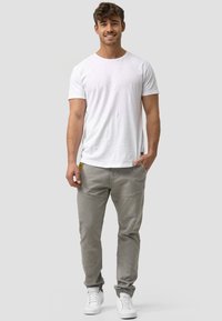 Weißes Baumwoll-T-Shirt und graue Jeanshose, slim fit mit dezenten Nähten, kombiniert mit weißen Sneakern, vor einem grauen Hintergrund stehend.