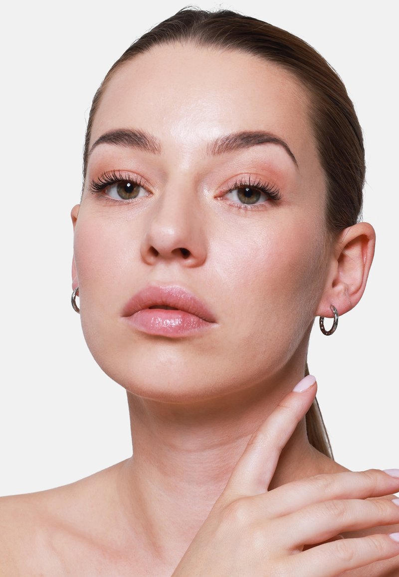 Orecchini a cerchio in argento indossati da una persona, con una superficie lucida e accenti texture. La pelle della persona ha un colorito naturale e levigato.