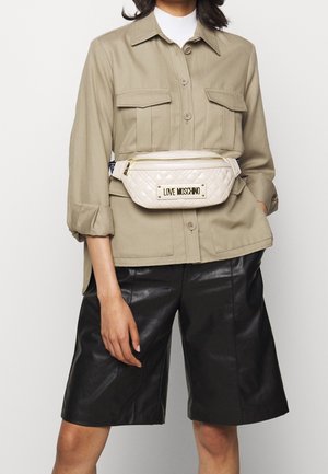 Beige button-up shirt with chest pockets, paired with black leather shorts. Front-worn quilted cream fanny pack features gold logo.