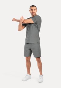 Conjunto deportivo para hombre en gris, que incluye una camiseta de manga corta y pantalones cortos. Tela texturizada, ajuste holgado, combinado con zapatillas blancas.