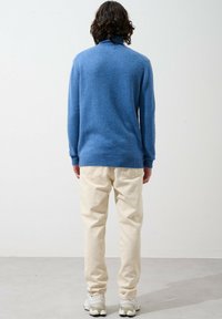 Svetle modrý pletený svetr s vysokým límcem a žebrovanými manžetami, kombinovaný s krémovými kalhotami se zúženým střihem a bílými teniskami.