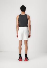 Débardeur gris pour homme associé à un short à côtes blanches, des chaussettes noires et des baskets rouges. Accent sur la coupe et les matériaux. Design minimaliste.