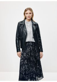 Czarna skórzana kurtka motocyklowa z srebrnymi detalami, noszona na szarym swetrze w warkocze i ciemnej kwiatowej spódnicy plisowanej.