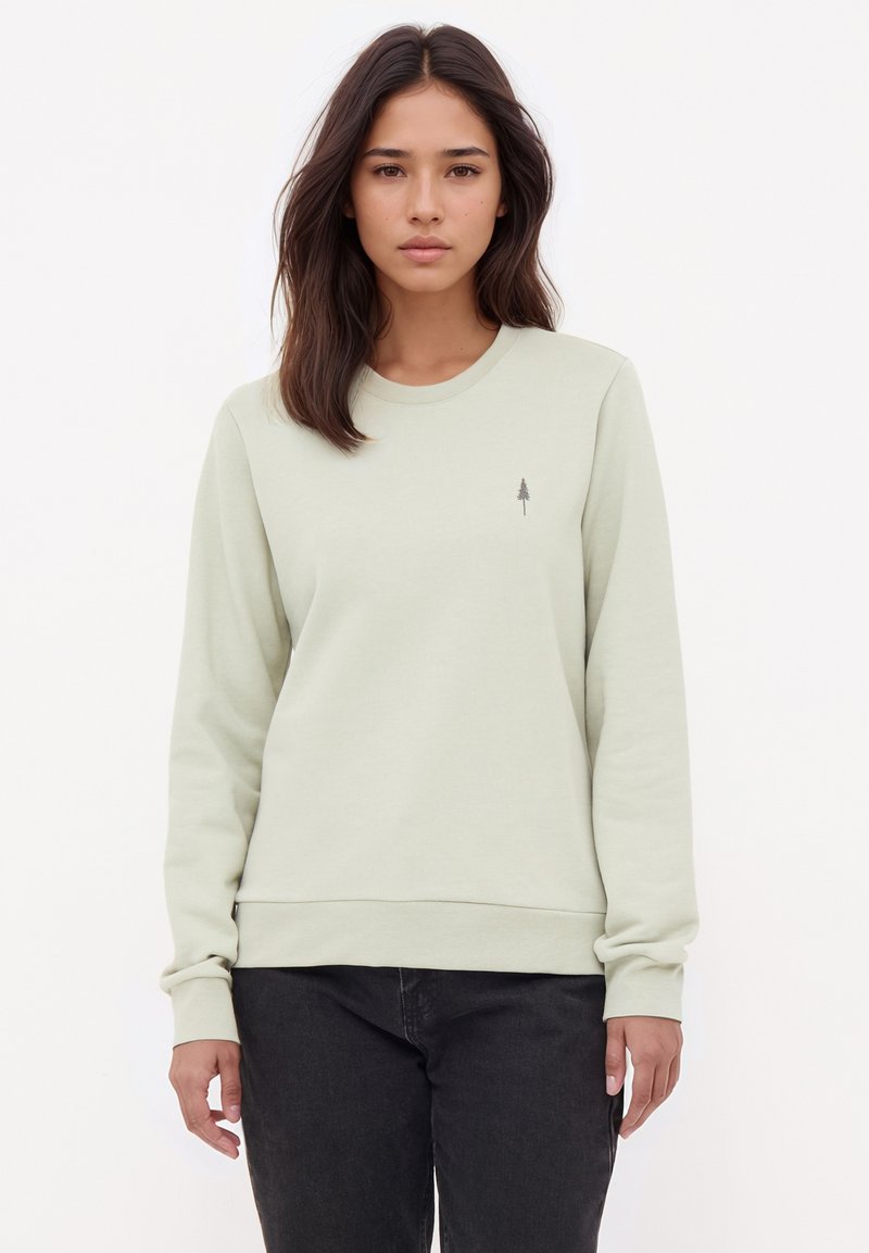Hellgrüner Pullover mit gerippten Bündchen und Saum, der ein kleines graues Baumlogo auf der linken Brust trägt. Weicher, glatter Stoff.