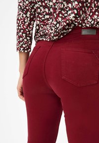 Jean skinny bordeaux en tissu doux, dotés de deux poches arrière et de détails de couture, associés à un haut à motifs.