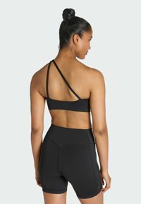 Crop top sportivo nero con texture a costine e design a spallina asimmetrica, abbinato a pantaloni corti neri a vita alta con dettagli nelle cuciture.