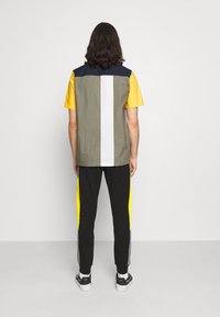 Kortärmad tröja med färgblockering i olivgrön, gul och marinblå, matchad med svarta byxor med gula och grå sidosträck.