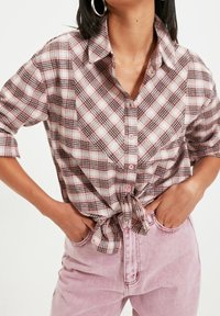 Camicia a quadri rosa e bianca con orlo annodato, abbinata a pantaloni di denim rosa. Presenta maniche lunghe e colletto.