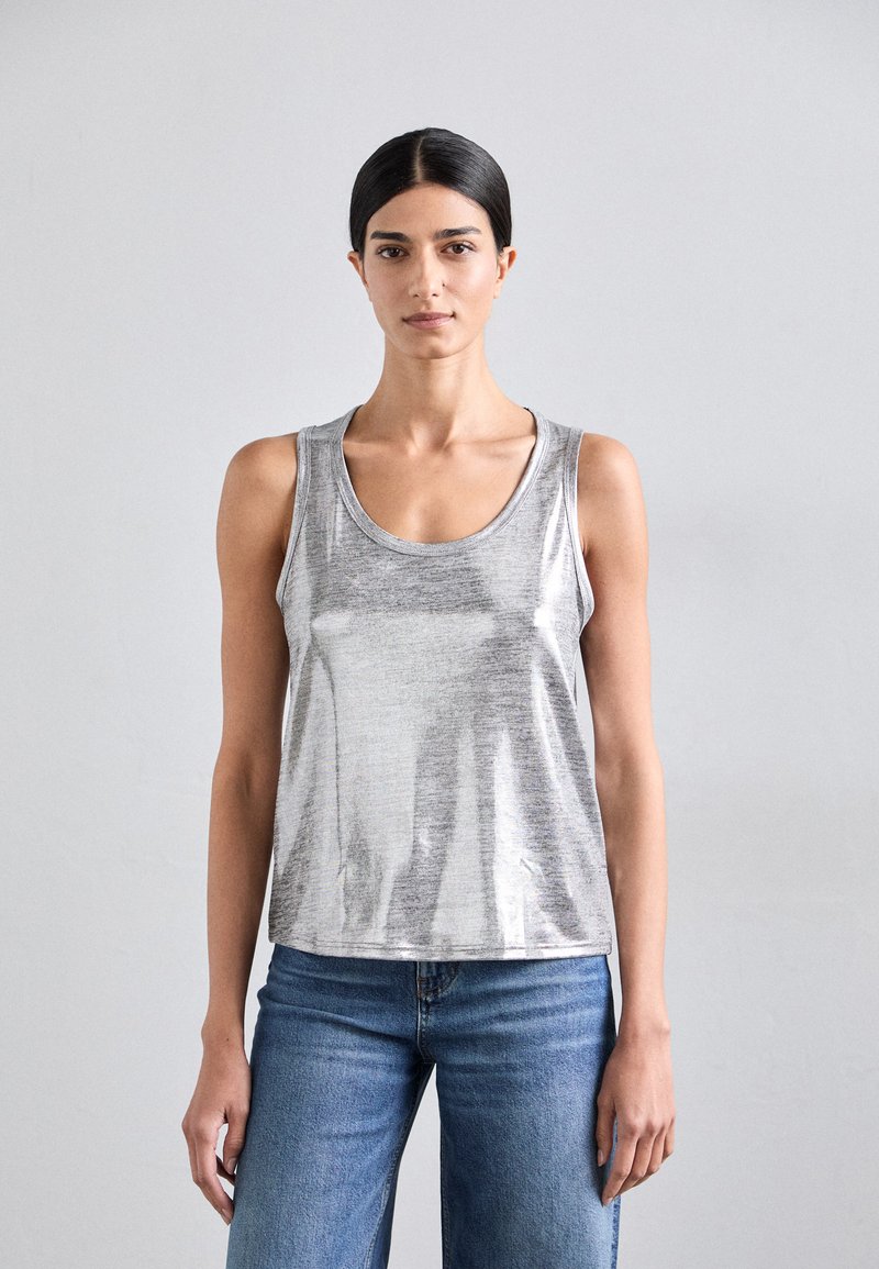 Silberner, metallischer Tanktop mit tiefem Ausschnitt und lockerer Passform. Der Stoff hat eine glatte Textur und einen subtilen Glanz. Kombiniert mit blauen Jeans.