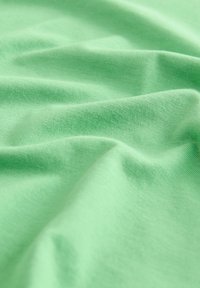 Tessuto verde chiaro con una texture liscia, che mostra morbide pieghe e drappeggi, indicativi di un materiale in cotone leggero.