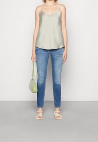 Satin, ljusgrön cami med tunna band; i kombination med blå, slim-fit jeans. Tillbehören inkluderar en liten, ljusgrön väska och vita sandaler.