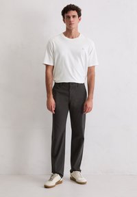 Biała koszulka z okrągłym dekoltem, ciemnoszare spodnie o prostych nogawkach oraz kremowe tenisówki. Koszulka ma małe logo; spodnie są gładkie.