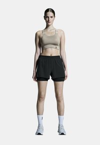 Beige sportbeha met verstelbare bandjes, gecombineerd met zwarte shorts met een binnenvoering. Grijze sportschoenen en witte sokken.