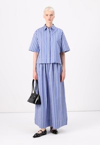 Camicia a maniche corte a righe blu e bianche e gonna maxi coordinata. Borsa nera e scarpe basse con dettagli circolari.