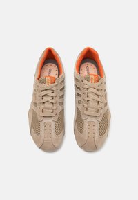 Beige idrettssko laget av semsket skinn og mesh-materialer, med oransje detaljer og perforeringer for ventilasjon; snøring.