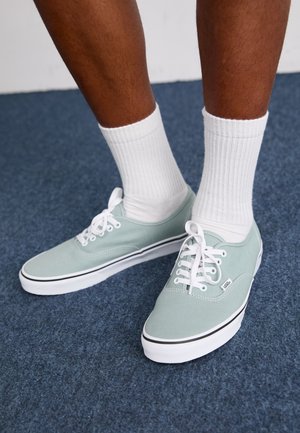 Mintgrønne lærredssko med hvide detaljer og snørebånd, der har en sort stribe langs sålen. Båret med hvide ribbede sokker.