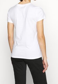 Biała bawełniana koszulka z krótkimi rękawami i okrągłym dekoltem, widziana od tyłu, ukazująca gładką fakturę i luźne dopasowanie.