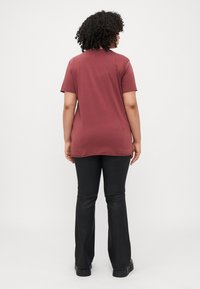 Maroon t-shirt with short sleeves and a relaxed fit, paired with black flared pants. Smooth texture, minimal detailing, and crew neck design.