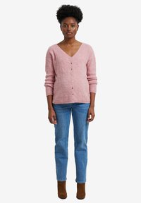 Rosa Strickjacke mit V-Ausschnitt, die ein strukturiertes Muster und sechs Knöpfe vorne aufweist. Kombiniert mit blauen Jeans und braunen Stiefeletten.