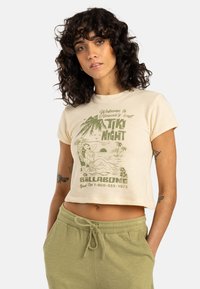 Cream-colored cropped t-shirt featuring a green retro graphic design with palm trees and a woman on the front. Soft texture, short sleeves.