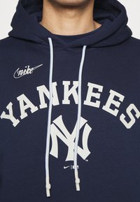 Sweat à capuche bleu marine avec texte blanc "YANKEES", logo des New York Yankees et logo Nike blanc sur la poitrine, porté par une personne.