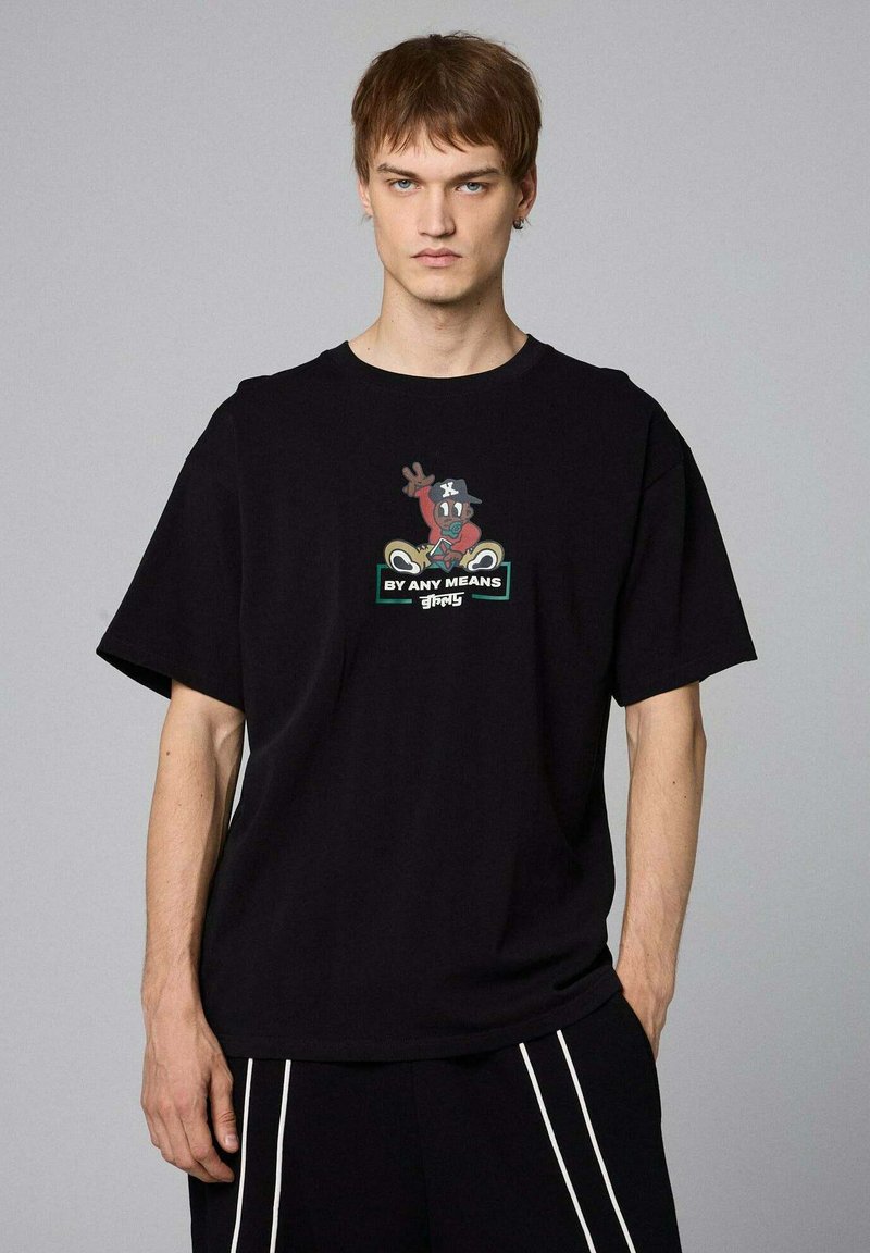 Camiseta de algodón negra con un diseño gráfico colorido de un personaje mostrando un signo de la mano y el texto "DE CUALQUIER MANERA" debajo.