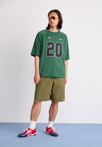 Green mesh t-shirt with black number 20, olive shorts, red and black sneakers, white socks, and mirrored sunglasses. Simple athletic design.