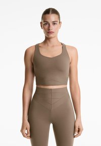 Smeđi crop top s V-izrezom i širokim naramenicama, u paru s tajicama visokog struka koje imaju geometrijsku teksturu i dizajn.