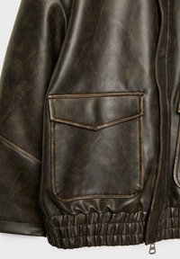 Giacca in pelle marrone con una texture liscia, caratterizzata da due tasche a patta e orlo elasticizzato. Cuciture dettagliate lungo le cuciture.