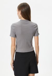 Grå ribbet kortærmet top med høj hals, parret med sorte shorts med sidelommer, der fremhæver en tætsiddende silhuet.