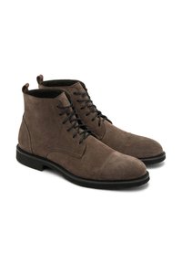 Brązowe zamszowe botki za kostkę z czarnymi sznurówkami, okrągłym noskiem i noskiem w formie cap toe. Posiadają płaską gumową podeszwę oraz uchwyty przy pięcie.