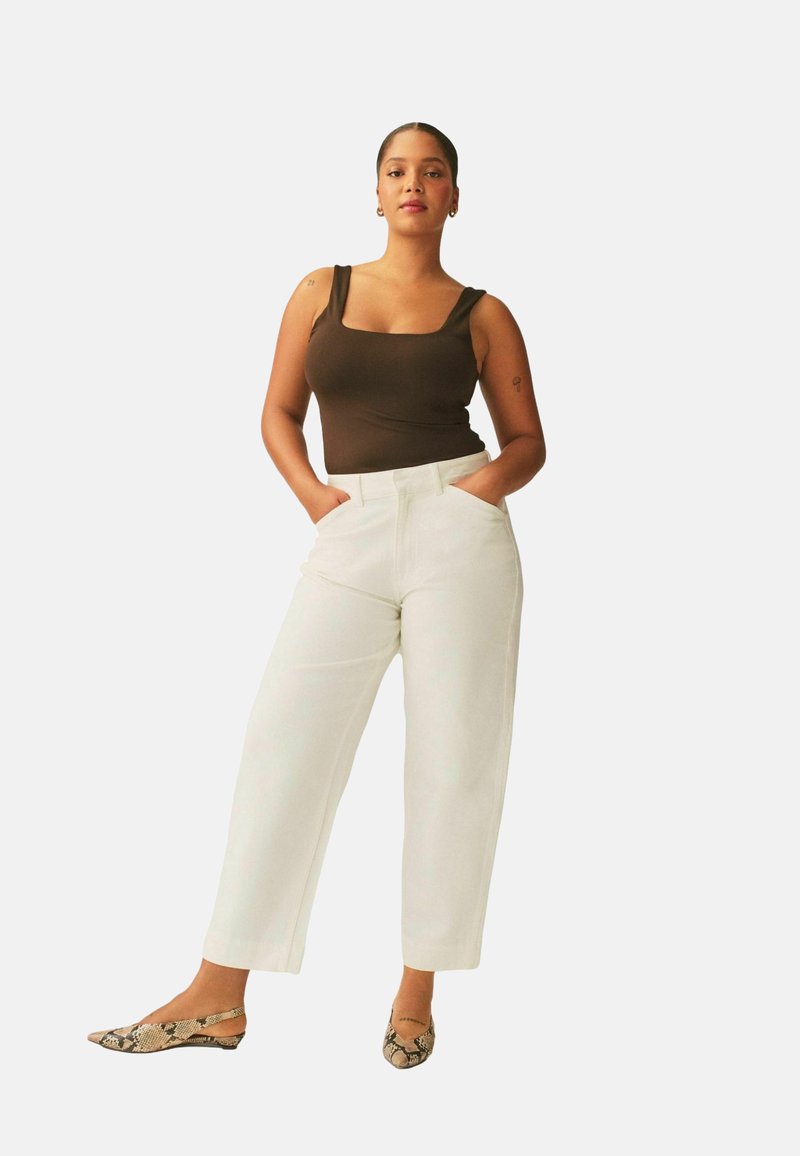 Ruskea neliskanttikaula-aukollinen toppi, valkoiset leveälahkeiset housut ja kuviolliset slingback-kengät. Yksinkertainen muotoilu, vähän yksityiskohtia.