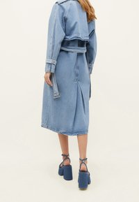 Denimjacka med figursydd midja och kluven bak. Ljusblå färg, strukturerad krage, långa ärmar med uppvikta manschetter och knytbälte.