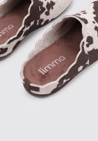 Slippers de fieltro con patrón marrón y blanco, con borde en forma de concha. Interior suave con suela marrón. Logo impreso en la plantilla.