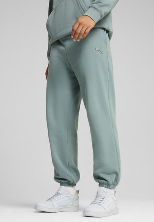 Light green sweatpants made of soft fabric, featuring elastic cuffs and a small embroidered logo. Paired with white high-top sneakers.