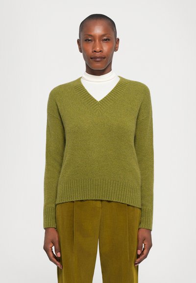 Grüner V-Ausschnitt-Pullover mit geripptem Saum und Bündchen, aus weichem Material, kombiniert mit olivgrünen Cordhosen. Einfaches Design und strukturierte Oberfläche.