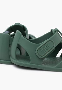 Sandalias verdes de material flexible, con talón cerrado, tira ajustable, plantilla texturizada y acento de logo en la tira.