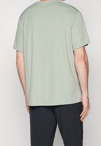 Světle zelené tričko s krátkým rukávem, kulatým výstřihem a volným střihem, vyrobené z měkké látky, kombinované s tmavými šortkami.